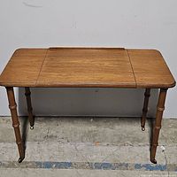 Front view of vintage wooden desk with solid rectangular top on turned legs with wheels.