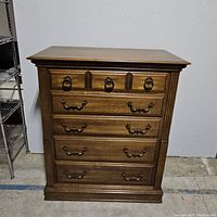 Front view of the vintage wooden dresser showing five drawers with metal handles and decorative molding.