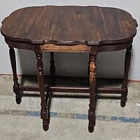 Full view of the vintage wooden table showing carved apron and turned legs with a scalloped tabletop edge.