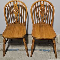 Front view showing pair of vintage wheelback Windsor chairs with curved backs and decorative central backrest cutouts.