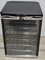 Front view of wine cooler showing glass door with metal racks inside and control panel above door handle.