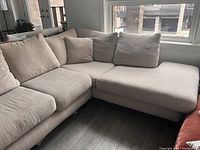 Left side view of beige sectional sofa with cushions and pillows, showing fabric texture and seat area.