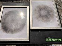 Two framed abstract sunburst prints placed outdoors on a black surface.