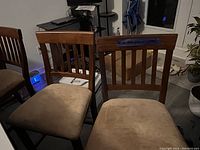 Four wooden bar height chairs with vertical slat backs and beige upholstered cushions shown from the front and side angles.