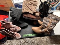 Photo of assortment of women's boots arranged on a flat surface, showing various styles, colors and materials including suede, knit, and leather-like materials.