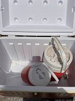Open white Igloo cooler showing interior and two red-and-white insulated jugs inside.