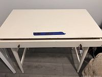 Front view of white wooden desk with single drawer and legs visible.