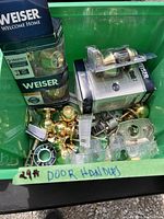 Various door handles, locking mechanism parts, and a Weiser Powerbolt keypad lock in original packaging along with other loose hardware items in a plastic bin.