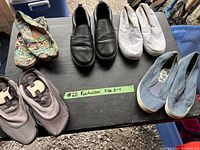 Five pairs of footwear arranged on a table, size 8-9 indicated on a label.