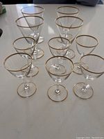 Ten clear stemmed glasses with a thin gold band around the rim and base, arranged in rows on a white surface.