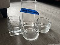 Four assemblies of clear glassware on floor: two square containers (one tall, one short) and two round containers (one medium, one small)