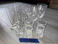 Thirteen clear glassware pieces arranged on floor including several champagne flutes, wine glasses, and two decorative ridged glasses with starburst bases.