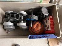 Photo showing a plastic container filled with gym equipment including adjustable dumbbells, an ab roller, a mini basketball, grip strengthener, and a boxed item.