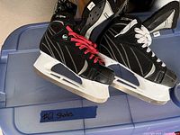 Pair of black hockey ice skates with white and red laces resting on a blue plastic container.