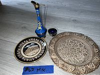 Photo showing two decorative plates, a tall blue ceramic vase, and a matching small blue cup placed on a floor.