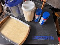 Two cans of Easy-Off spray cleaner (new), a Brita water pitcher with blue lid, a white Tupperware pitcher, and a vintage wooden-handled tray with a light surface area.