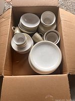 Box of Pfaltzgraff stoneware dishes showing a variety of plates, bowls, cups, and saucers in beige/cream color.