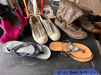Photo of five pairs of women's shoes in sizes 8-9, including boots, sneakers, sandals, and flip-flops arranged on a surface.