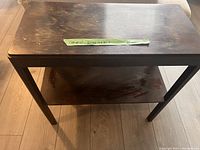 Photo of brown wooden side table showing top surface and lower shelf with visible wear and marks