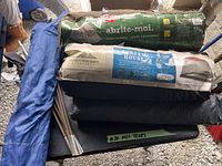 Photo showing stacked camping tents in their storage bags, labeled with brand names 'abrite-moi' and 'Northwest Territory Screen House,' alongside bundled tent poles and tarps.