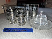 Photo showing six small etched glasses, five tall etched highball glasses, and a clear glass butter dish with dome lid. Glassware features silver-tone decorative etching.
