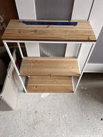 Photo of three-tier wall shelf with white metal frame and natural wood shelves, showing condition and design.