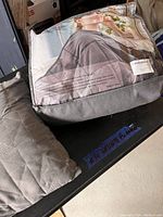 Photo of a folded weighted blanket in packaging along with a quilted gray pillow beside it.