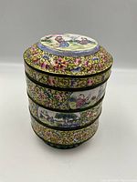 Assembled tiffin box, front view showing floral scrollwork and figurative panels on four stacked tiers