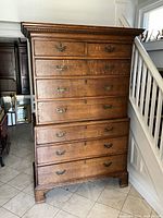 Full front view of antique oak tallboy chest of drawers against a staircase background