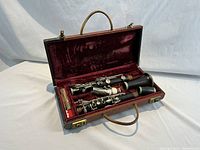 Open carrying case showing disassembled clarinet inside the red velvet lining and a cleaning swab or cloth