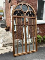 Full front view of entire mirror leaning against brick wall outdoors