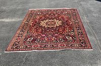 Full view of rectangular rug laid flat on asphalt, showing central medallion and overall pattern