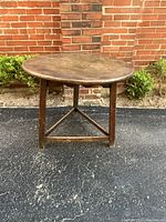 Front view of round oak table on triangular base against brick wall