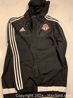 Front view of black Adidas jacket with white sleeve stripes and Toronto FC logo embroidered on left chest.