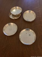 Photo of 4 Birks sterling silver round coasters arranged on wood surface, showing plain polished finish and subtle raised rims.