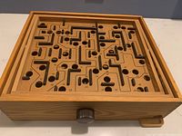 Top-down view of the BRIO wooden labyrinth maze game showing maze pathways, numbered holes, and wooden control knob on the side.