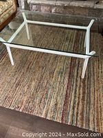 Angled side view showing white aluminum legs and the clear tempered glass top of the coffee table on a multi-color rug.