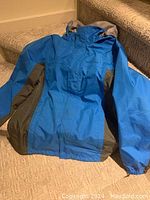 Front and part of jacket details showing blue and dark olive green color blocking, hood, elastic cuffs, and WeatherEdge logo on chest.