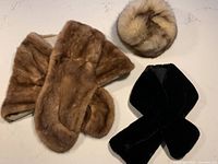 Three fur accessories displayed on a white surface: brown mink fur stole with lining, round fox fur hat, and black faux fur neck wrap.