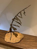 Full side view of the twisted iron branch sculpture mounted on an irregular granite rock, showing the overall shape and height.