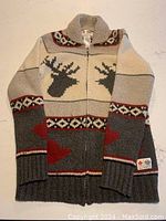 Full front view of the zip-up sweater cardigan showing reindeer and heart motifs, knit collar, ribbed cuffs and hem, in grey, cream, and red colors.