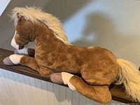 Side profile of large brown and white stuffed horse, lying down with cream mane and tail visible.