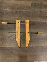 Top view of the wooden vice clamp lying on a wooden floor, showing overall design with two handles and jaws.