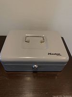 Top view of white rectangular metal cash box with handle and Master Lock logo.