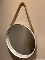 Front view of the circular mirror hanging on the wall showing the steel frame and rope hanger.