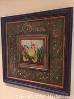Square folk art painting on pine boards featuring a yellow rooster and two chicks in tall green grass, surrounded by a decorative multicolored raised inset frame