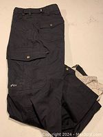 Photo of folded black ROXY snowboard pants with visible buttoned cargo pocket and ROXY logo on thigh pocket.