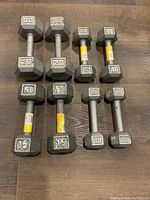 Photo showing four pairs of hexagonal cast iron dumbbells arranged on a floor. The pairs are weighted 8, 10, 15, and 20 pounds respectively.