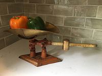 Front view showing scale with two bell peppers on brass pan, orange base, and balance arm with brass weight.