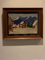 Front view of the framed hooked rug showing the Quebec winter scene with houses, snow, and mountains.